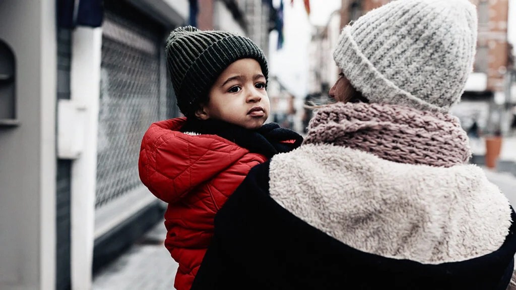 Vue arrière de maman marchant dans la rue portant un petit bébé dans ses bras - Lumière du jour d'hiver