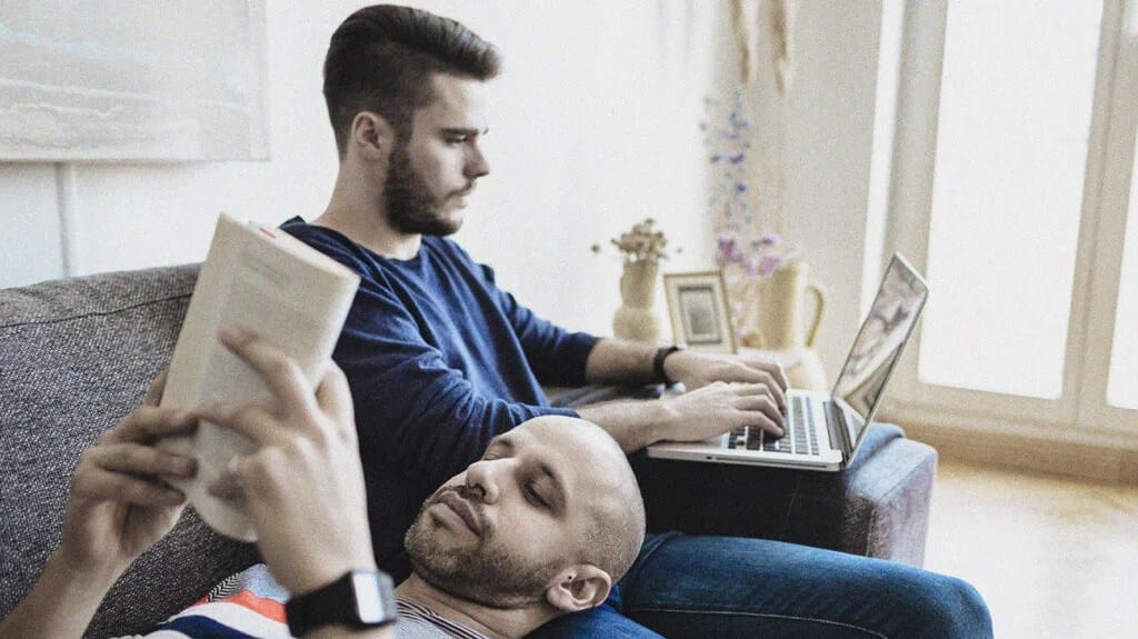 deux hommes prenant une journée de repos après l'exercice se détendent sur un canapé pendant que l'un d'eux lit un livre