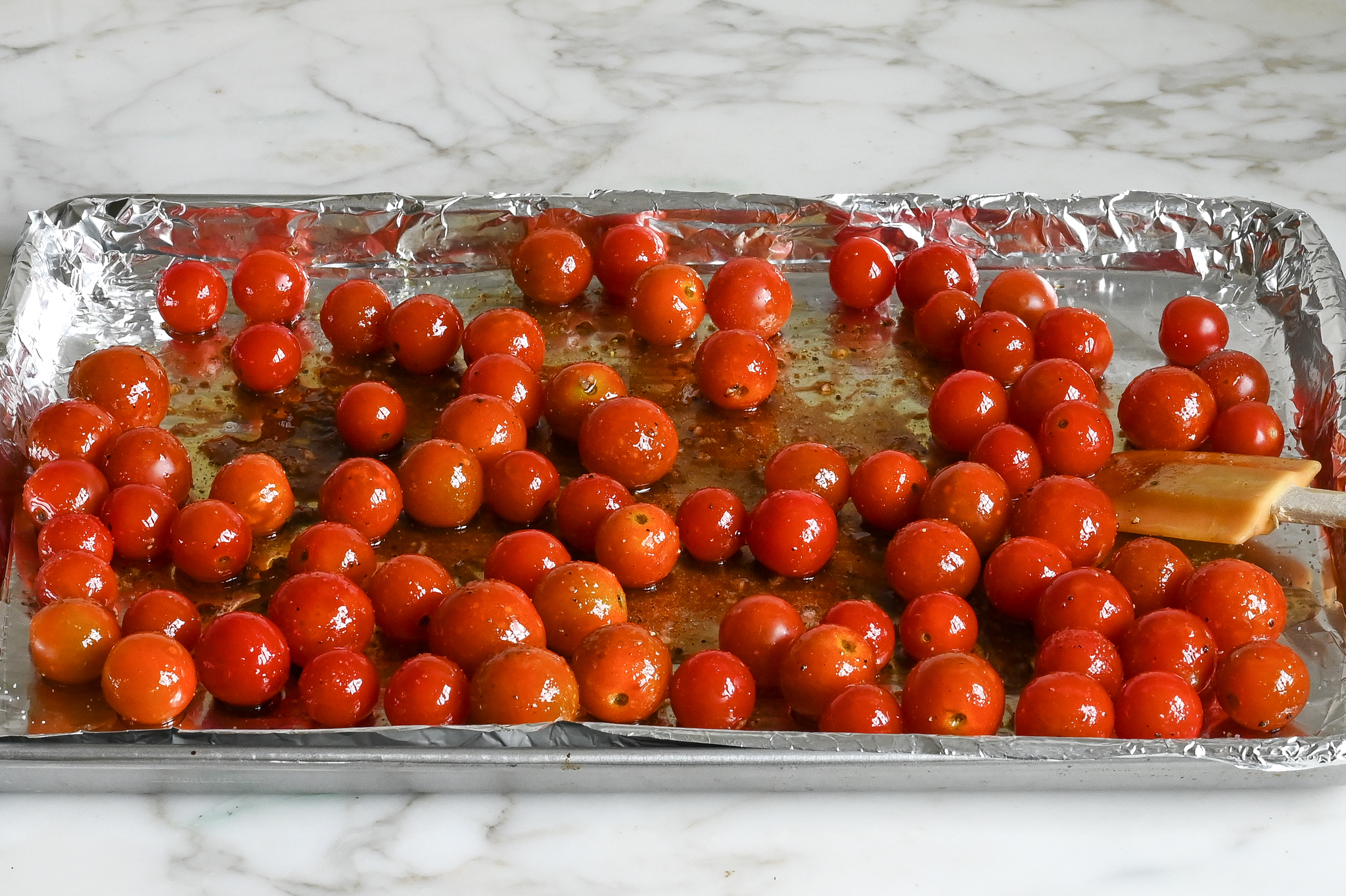 tomates cerises mélangées à de l'huile, du vinaigre, de l'ail et des assaisonnements et prêtes à rôtir