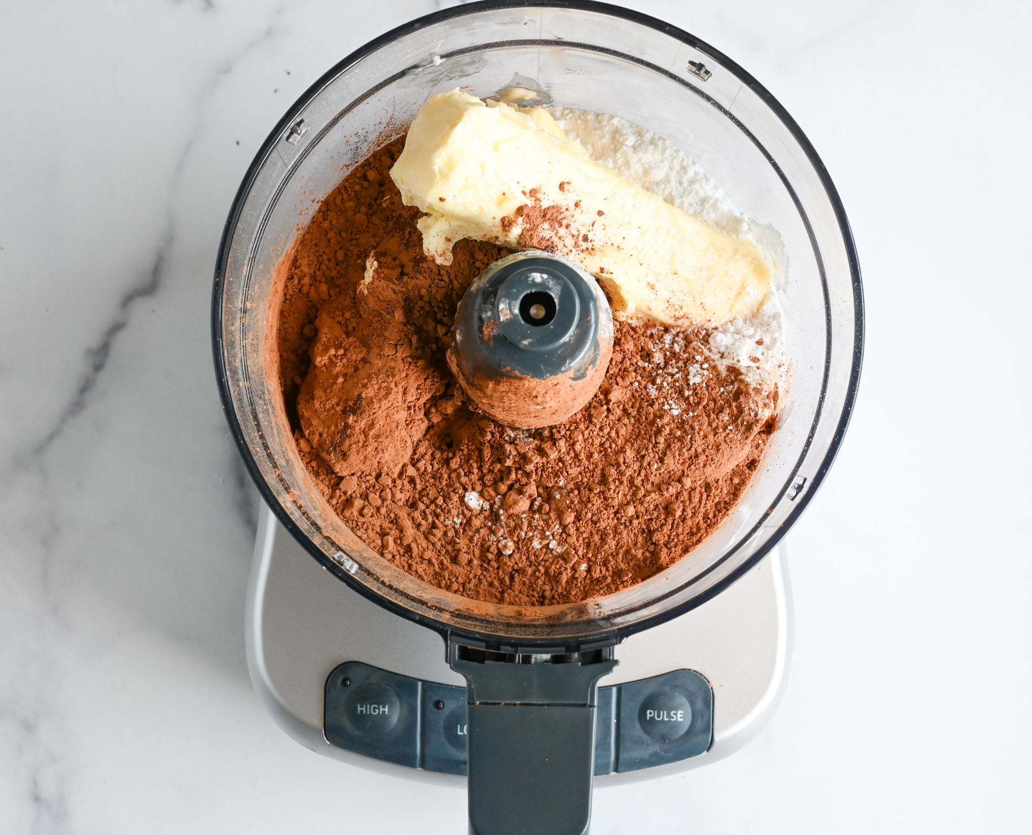 beurre, sucre glace et poudre de cacao dans un robot culinaire